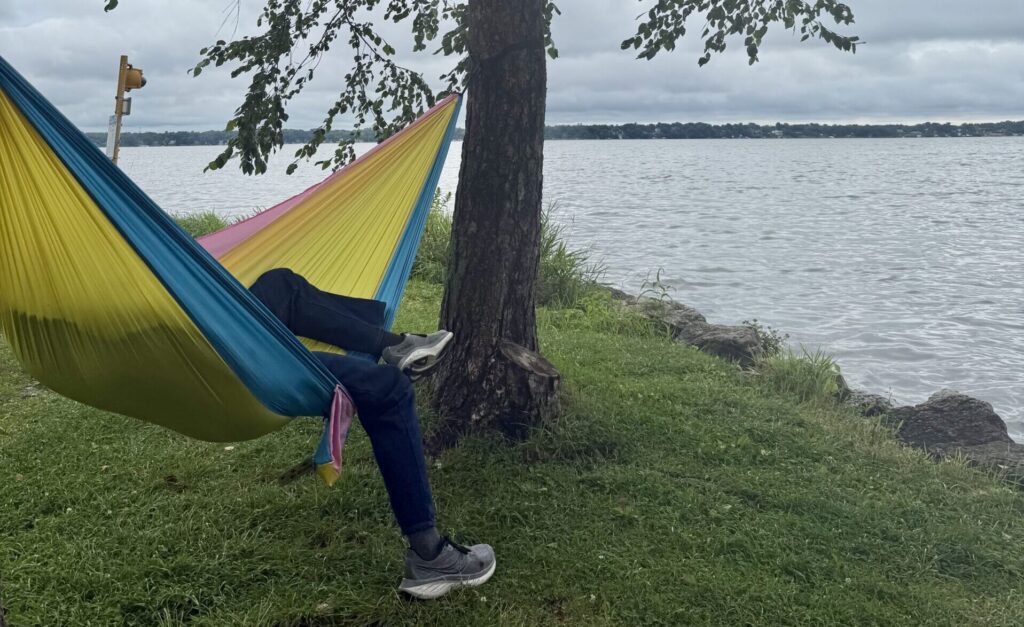 Person's legs hanging out of a bright colorful hammock overlooking the water.