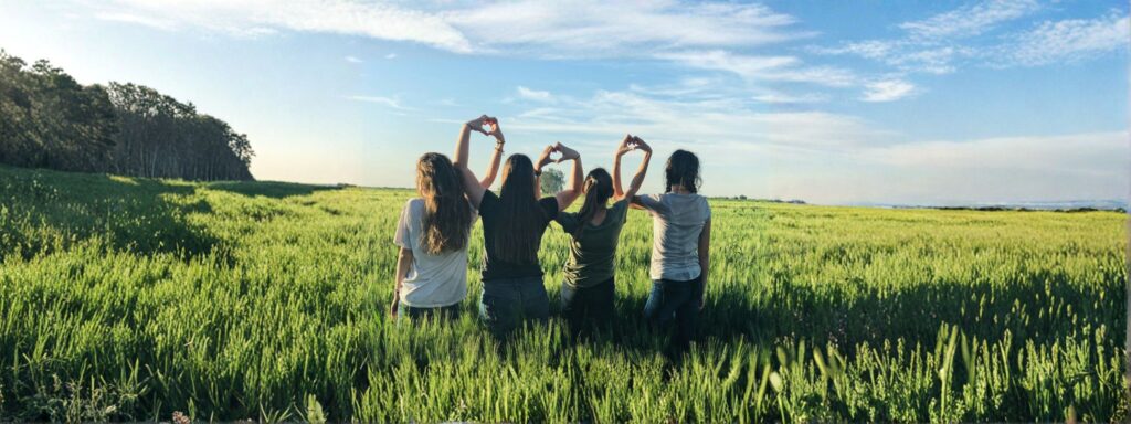 Group of young people standing together in a field, forming heart shapes with their hands.
